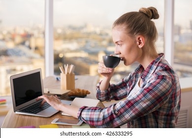 Casually Dressed Female Enjoying Coffee Using Laptop Computer. Hipster Woman Drinking Coffee While Waiting For Mail On Her Laptop. Hardworking Woman Getting Work Done On Laptop Over Cup Of Coffee