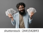 A casually dressed man stands against a neutral background, holding a wad of cash with both hands. The image conveys concepts of wealth, finance, savings, and success without showing the man