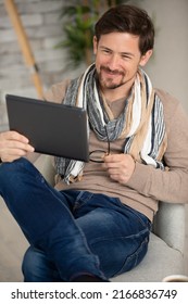 Casually Dressed Man Using Tablet Sat On The Sofa