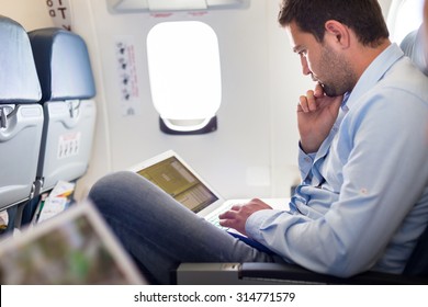 Casually dressed middle aged man working on laptop in aircraft cabin during his business travel. Shallow depth of field photo with focus on businessman eye.