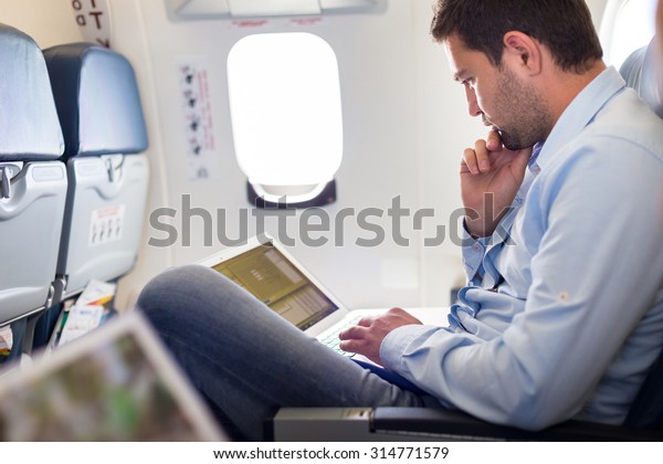 Casually dressed middle aged man working
on laptop in aircraft cabin during his business travel. Shallow
depth of field photo with focus on businessman
eye.