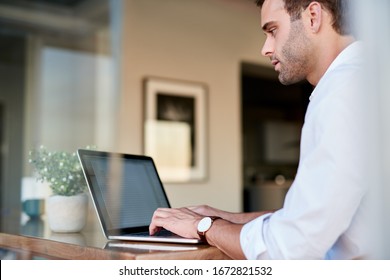 Casually Dressed Young Businessman Sitting Alone At At His Dining Table At Home Working Online With A Laptop