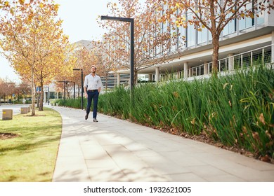 Casually Dressed Young Businessman Walking Outside On A Footpath By An Office Complex In Autumn