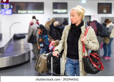 Casually dressed young female traveller waiting in airport arrival terminal hall,  collecting her laggage . Blured background. Can also be used as railway, metro, bus station.