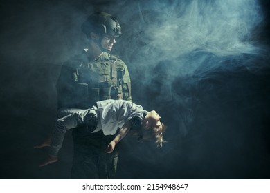 Casualties of war. Portrait of a courageous soldier carrying a little girl in his arms injured in war zone. Studio portrait on a dark background with smoke. Copy space.