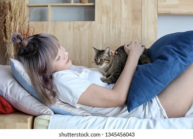 Cat Lover Concept. Beautiful Asian Woman Sitting On Sofabed And Carrying A Cat On His Hand With Love. Cute Girl And Cat.