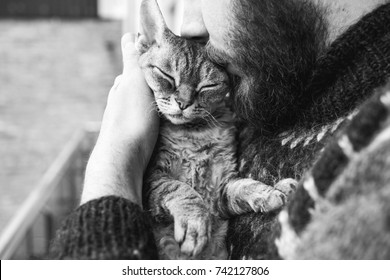 Cat and man, portrait of happy cat with close eyes and young man. Handsome Young Animal-Lover Man, Hugging and Cuddling his Gray Domestic Cat Pet. Black and white photo.