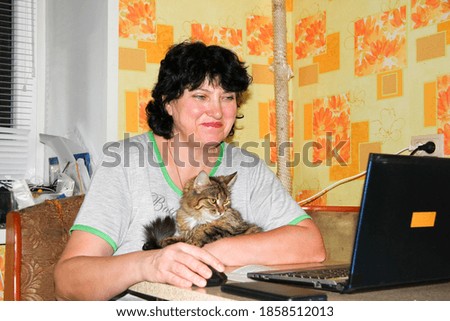 The cat is sheltered in the arms of a woman who works at home on a laptop.