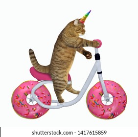 The Cat Unicorn Is Riding The Bicycle. The Wheels Look Like A Big Donuts. White Background. Isolated.