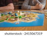 catan game pieces on a board on a table with family in background