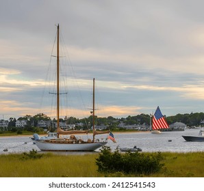 A catboat with American Flag sails by boats in Edgartown Harbor on the island of Martha's Vineyard