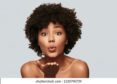 Catch!  Beautiful young African woman blowing a kiss while standing against grey background