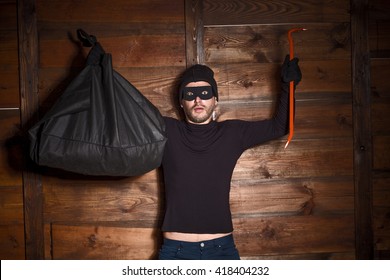 Catch Burglar Concept, Thief With Balaclava Caught In Front Of Wooden Wall Of Someone's House. Man Standing With His Hands Up. 