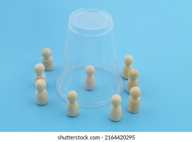Catch and isolation concept. Wooden people figures on blue background close-up. One figure under  plastic cup.