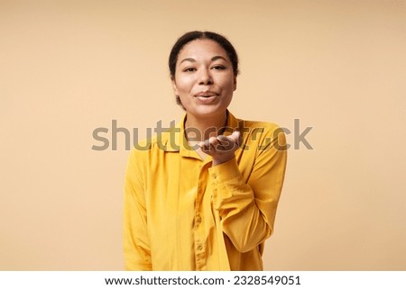 Catch my kiss. Lovely romantic african american girl looking at camera and air kissing over palms hands, sending love. Beauty care and fashion vogue. indoor studio shot isolated on beige background