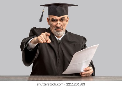 Catch In Plagiarism Concept. Angry Academician, Professor, Prof Is Wearing A Cap With Tassel And Black Gown Pointing Finger At The Camera. Senior Educator Learned Man From A University Or College.