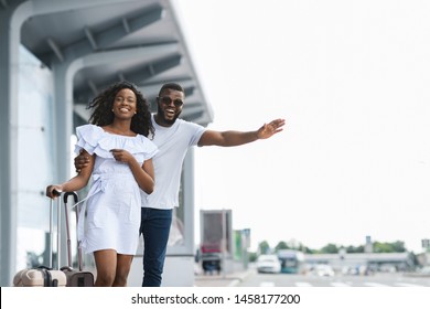 Catch taxi. Young african couple standing near airport, man raising hand and trying to stop car, empty space - Powered by Shutterstock