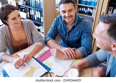 Catching Up On The News. High Angle Shot Of Three Coworkers Talking Around A Table.