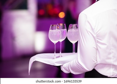 Catering Or Celebration Concept. Waiter Or Waitress Holding A Tray With Glasses Of Cocktails Or Sparkling Wine At Reception Party, Beverages. Blurred Background.