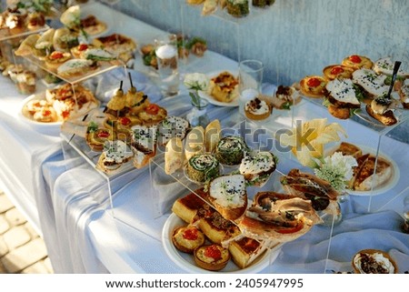 catering. Lavish spread of assorted appetizers displayed on white cloth-covered table, wraps visible fillings, canap�topped with different toppings arranged on clear stands, yellow flower in focus