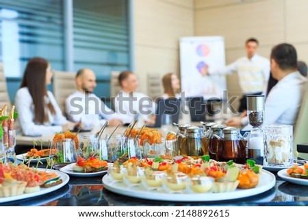 Catering in the office. A table with canapes and various snacks served  on the background of a business meeting