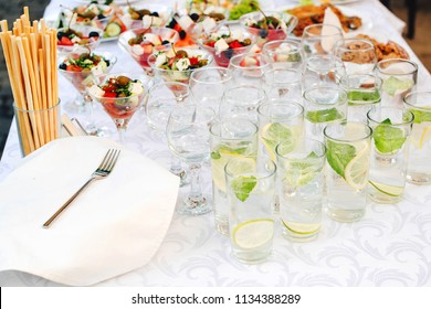 Catering For Outdoors Party. Catering Buffet Food On Some Festive Event, Party Or Wedding Reception. Water With Lemon And Mint. Greek Salad In Glasses On Table, Banquet Food. Catering Service