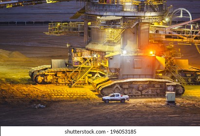 Caterpillats detail view of a giant Bucket Wheel Excavator next to a pickup truck at night