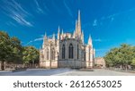 Cathedrale Saint-Andre de Bordeaux timelapse hyperlapse with twin spires under a vibrant blue sky. Green trees and people walking in the square create a serene urban atmosphere. Bordeaux, France