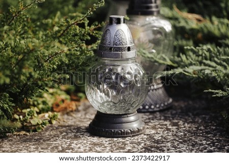 Catholic cemetery background. All saints holiday. Grave candle light. Halloween on graveyard. Grave candles on marble tomb. Gray granite grave. White grave candle. Conifers decoration forest tomb.