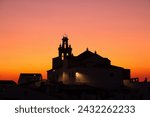 Catholic Church of Our Lady of the Flowers in Sanlúcar de Guadiana, Huelva, Spain. Silhouette of the church bell tower in an orange sky during sunset.