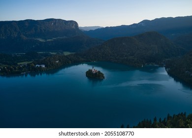 Catholic church situated on an island on the Bled lake with mountains and villages on the background