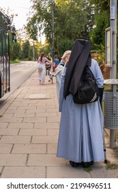 A Catholic nun in monastic garb at a bus stop talking to an elderly woman in Krakow, Poland, with bus passengers walking down the sidewalk ahead - Shutterstock ID 2199496511