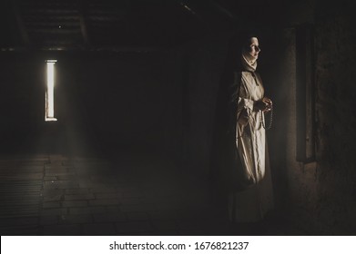 Catholic nun prays in the dark old church. Historical cosplay of vintage church. A woman in old nun catholic cassock