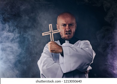 Catholic priest exorcist in white surplice and black shirt with cleric collar praying with crucifix - Shutterstock ID 1213050640