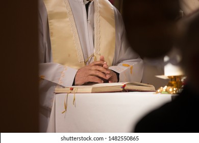 Catholic priest holding hands in prayer above a holy book during mass - Shutterstock ID 1482550865