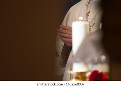 Catholic priest holding hands in prayer in front of a candle obstructed by a wall - Shutterstock ID 1482560309
