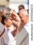 a catholic priest holding a host during the sacrament of communion at an outdoor service