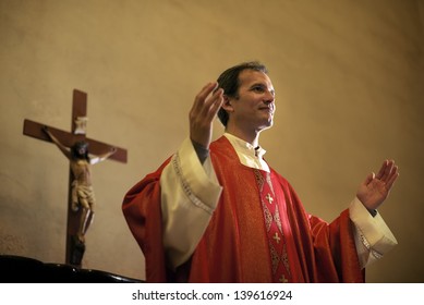 Catholic Priest On Altar Praying With Open Arms During Mass Service In Church