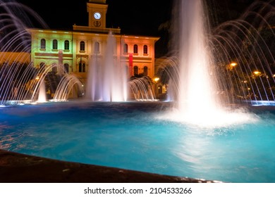 Cattolica, Italy - 04-08-2021: Illuminated And Colored Fountain With The Cattolica Town Hall In The Background