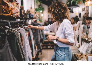 Caucaisan female customer with curly hair buying clothes in boutique using fitting concept while choosing, professional stylist creating trendy look concentrated on selection in designer shop - Powered by Shutterstock