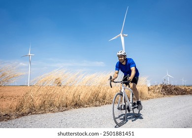 Caucasian active sportsman riding bicycle at the wind turbine field. Attractive athlete in sportswear exercise by cycling workout outdoors for health and wellness in rural area at windmill power farm. - Powered by Shutterstock