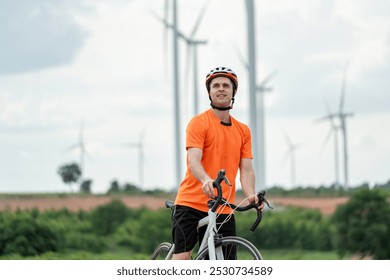 Caucasian active sportsman riding bicycle at the wind turbine field. Attractive athlete in sportswear exercise by cycling workout outdoors for health and wellness in rural area at windmill power farm. - Powered by Shutterstock