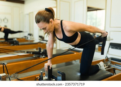 Caucasian active woman at a beautiful high end gym exercising taking a pilates class using a bed reformer doing ab workout - Powered by Shutterstock