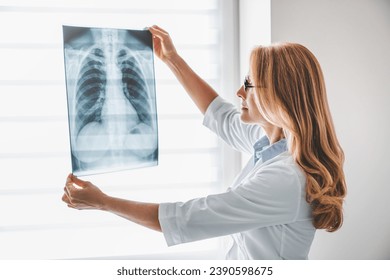 Caucasian adult female doctor looking at x-ray. Radiologist checking investigating patient`s lungs on image. Pneumonia, chest pain, coronavirus treatment