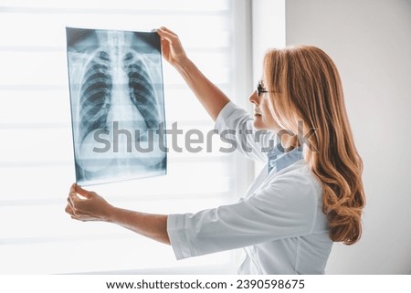 Caucasian adult female doctor looking at x-ray. Radiologist checking investigating patient`s lungs on image. Pneumonia, chest pain, coronavirus treatment