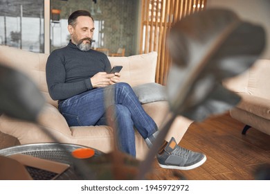 Caucasian Adult Man Is Sitting With Smartpone In Modern Cozy Office Lounge Zone