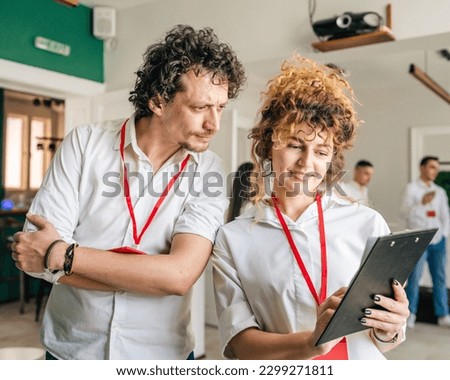 Caucasian adult man and woman stand at work wear white shirts holding a clipboard discuss business results happy smile on faces celebrate success productive and positive attitude towards work