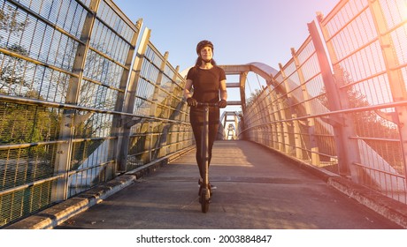 Caucasian Adult Woman riding an electric scooter on a path across a pedestrian bridge over the highway in a modern city. Taken in Fraser Heights, Surrey, Vancouver, British Columbia, Canada. - Powered by Shutterstock