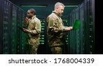 Caucasian and African American men in camouflage uniforms working in server room and checking data with tablet device and laptop computer. Mixed-races army forces co-workers Walkie-talkie info passing