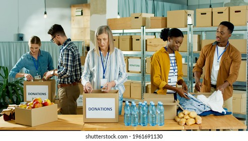 Caucasian and African American people men and women volunteers working at charity organization packing clothes and food grocery in donations box. Volunteering, social help for poor and needy - Powered by Shutterstock